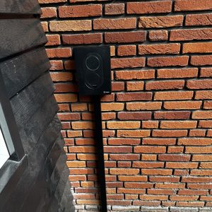 Een laadpaal is geïnstalleerd aan de muur van een gebouw, met een eenvoudige, moderne uitstraling.