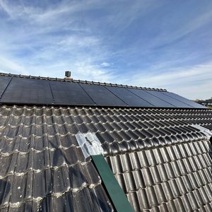 De foto toont een installatie van zonnepanelen op een hellend dak met traditionele dakpannen.