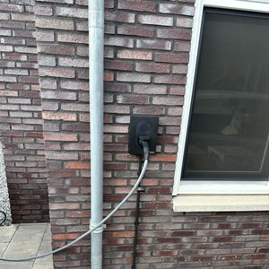 Een laadpaal voor elektrische voertuigen, stevig bevestigd aan een muur, uitgerust met een laadstekker en kabel.