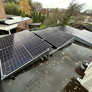 De foto toont een installatie van zonnepanelen op een schuin dak, met een donkere lucht en bladeren op het dak.