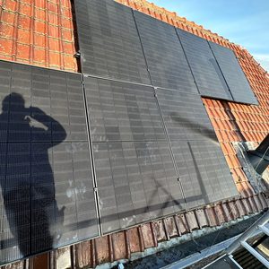 Zonnepanelen zijn geïnstalleerd op een dak met rode dakpannen, zichtbaar in de zon.