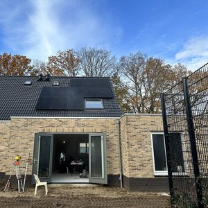 De foto toont een recente installatie van zonnepanelen op het dak van een woning, met een heldere hemel op de achtergrond.