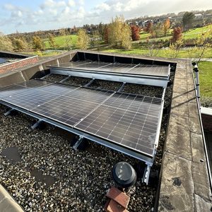 Deze installatie toont zonnepanelen op een plat dak, gemonteerd op een systeem met grind ter stabilisatie. De panelen zijn gericht op optimale zonreflectie.