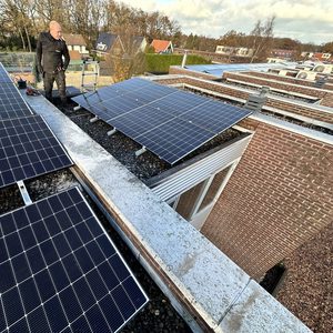 Deze installatie toont zonnepanelen op een plat dak, met een technicus die de panelen inspecteert en onderhoud uitvoert.