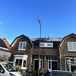 De afbeelding toont zonnepanelen geïnstalleerd op de daken van twee huizen, met een helderblauwe lucht op de achtergrond.