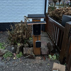 De afbeelding toont een laadpaal voor elektrische voertuigen, geplaatst naast een huis en omringd door natuurlijke elementen.