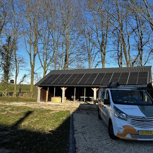 Een installatie van zonnepanelen op het dak van een houten bijgebouw, met een werkvoertuig op de voorgrond.