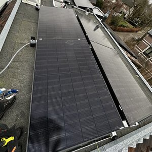 De afbeelding toont een zonnepaneleninstallatie op een dak, met meerdere zonnepanelen geplaatst en bekabeling zichtbaar.