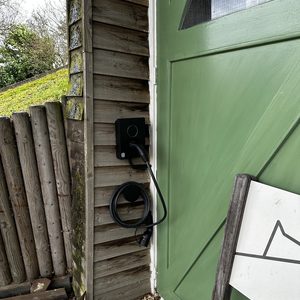 Een laadpaal is geïnstalleerd aan een wand, met een kabel hangend voor gebruik. De omgeving toont installatiegereedschap en materialen.