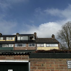 Zonnepanelen zijn geïnstalleerd op het dak van een rijtjeshuis, zichtbaar onder een gedeeltelijk bewolkte lucht.
