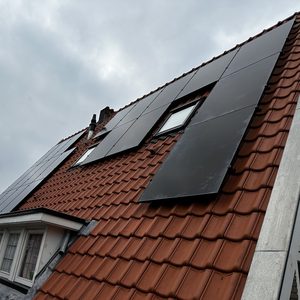 De afbeelding toont zonnepanelen die op een hellend dak zijn geïnstalleerd, met een grijze lucht op de achtergrond.