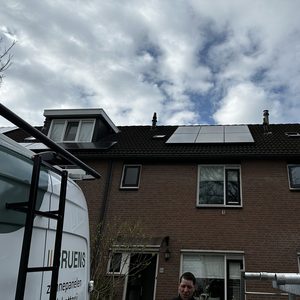 Deze installatie toont zonnepanelen op een dak van een woning, met een professional die werkzaam is in de buurt van de installatie.