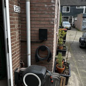 De laadpaal is gemonteerd aan de muur, met een kabelhaspel in de buurt en een verzorgde omgeving met plantenpotten.