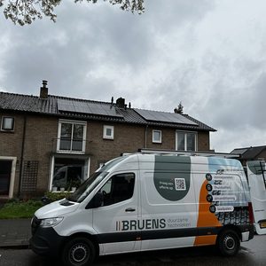 De foto toont zonnepanelen die zijn geïnstalleerd op het dak van een woning, met een bedrijfswagen van een installatiebedrijf op de voorgrond.