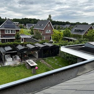 De afbeelding toont een residentieel dak met zonnepanelen die zijn geïnstalleerd, omgeven door een groene tuin en huizen in de nabijheid.