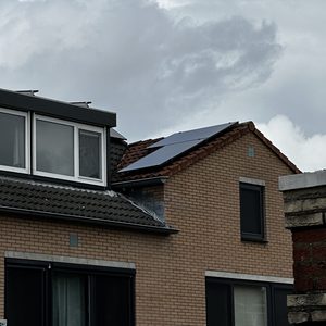 De afbeelding toont een woning met zonnepanelen op het dak, met een bewolkte lucht erboven.
