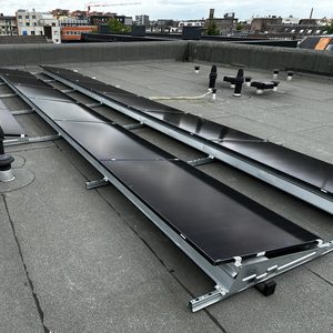 De foto toont een installatie van zonnepanelen op een plat dak, met meerdere panelen die zijn gemonteerd op een metalen frame.