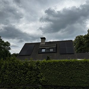 De installatie toont zonnepanelen op een schuin dak met een groene haag op de voorgrond.