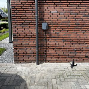 Een laadpaal is bevestigd aan de muur van een gebouw, klaar voor het opladen van elektrische voertuigen.