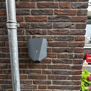Een laadpaal is geïnstalleerd aan een bakstenen muur, klaar voor elektrisch opladen van voertuigen.