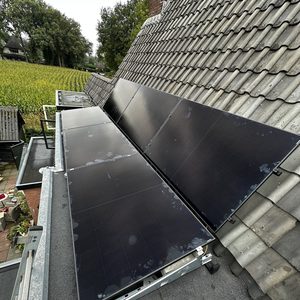 Deze installatie toont zonnepanelen die op een hellend dak zijn gemonteerd, met een zichtbare groene omgeving en dakpannen op de achtergrond.