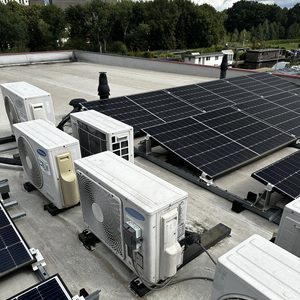 Een luchtconditioningsinstallatie op het dak, naast zonnepanelen. De unit is goed zichtbaar en klaar voor gebruik.