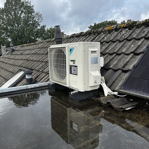 Een luchtconditioningsunit geïnstalleerd op een dak, met zichtbare reflectie in water en omliggende zonnepanelen.