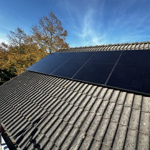 Een installatie van zonnepanelen op een hellend dak, met een heldere blauwe lucht op de achtergrond.