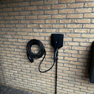 Een laadpaal voor elektrische voertuigen met een kabel op een muur gemonteerd, klaar voor gebruik.
