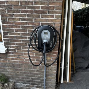 Een moderne laadpaal voor elektrisch voertuigen, bevestigd aan de muur, met een oplaadkabel die netjes is opgerold.