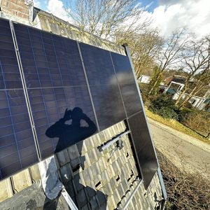 Installatie van zonnepanelen op een schuin dak, met meerdere panelen zichtbaar en een heldere lucht op de achtergrond.