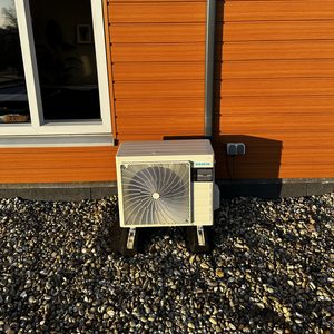 Een buitenunit van een airconditioningssysteem, gemonteerd tegen een houten wand met een zichtbare afvoerleiding.