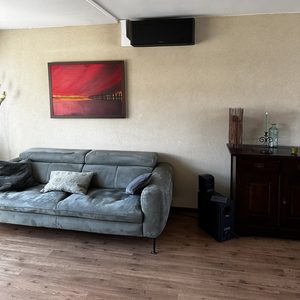 Een wand-airconditioner geïnstalleerd in een woonkamer, boven een bank, met een kunstwerk op de muur.