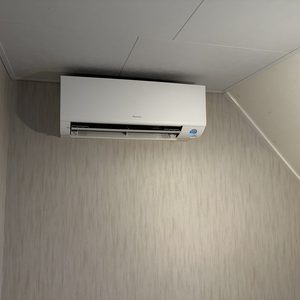 Een wandmodel airconditioner is geïnstalleerd in een kamer, met een moderne uitstraling tegen een neutrale muur.