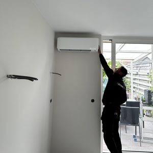 Een monteur installeert een airconditioningseenheid aan de muur in een moderne woonruimte.