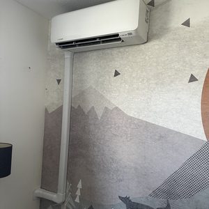 Een wandgemonteerde airconditioningseenheid met leidingen en een stijlvolle achtergrond.