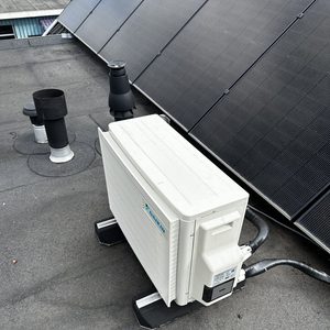 Deze foto toont een airconditioningseenheid geplaatst op een dak, naast zonnepanelen.