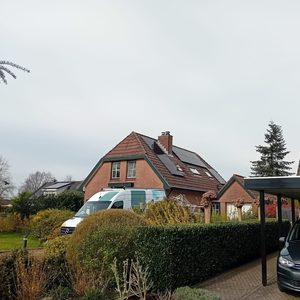 De foto toont een woning met zonnepanelen op het dak, omgeven door tuin en voertuigen.