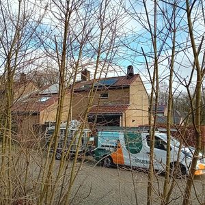 De afbeelding toont een huis met zonnepanelen op het dak, omringd door bomen en een werkvoertuig van een installatiebedrijf.