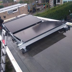 De afbeelding toont een technicus die zonnepanelen installeert op een plat dak, met een ladder voor ondersteuning.