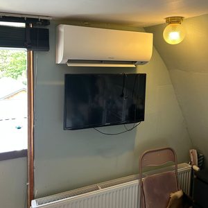 Een wand airco-unit is geïnstalleerd boven een televisie, met een radiator eronder in een woonkamer.