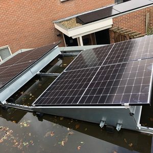 Installatie van zonnepanelen op een dak, zichtbaar met reflectie in water en omgevingsplanten.