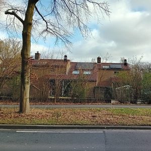 De afbeelding toont een woning met zonnepanelen geïnstalleerd op het dak, omringd door vegetatie.