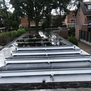De foto toont zonnepanelen op een plat dak die zijn geïnstalleerd op een systeem met rails.