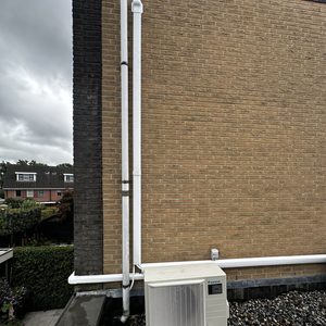Een wandgemonteerde airconditioning unit op een plat dak, met bijbehorende leidingen voor koeling en verwarming.