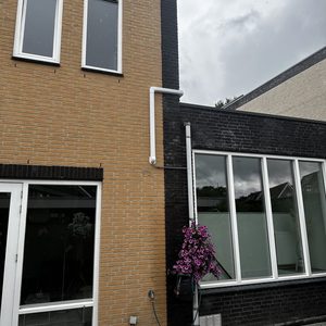De foto toont een installatie van airconditioning met leidingen aan de buitenkant van een woning, naast een bloemstuk.