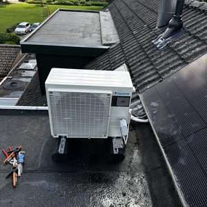 Een Daikin airco-unit geïnstalleerd op het dak, met gereedschap ernaast voor het onderhoud of de installatie.