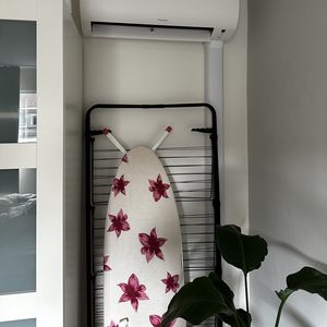 Een wandgemonteerde airconditioner in een woonruimte, met een strakke uitstraling en een kledingrek op de achtergrond.