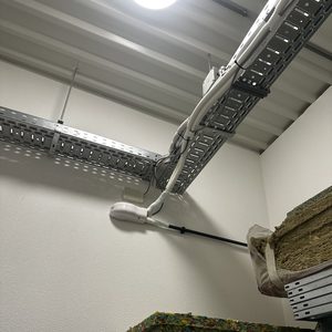 De afbeelding toont een airconditioninginstallatie met leidingen en een unit, net boven een rek met materialen.