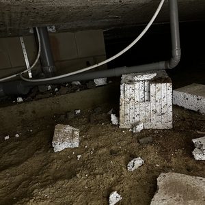 Een airco-installatie project zichtbaar onder een gebouw met leidingen en afval op de grond.